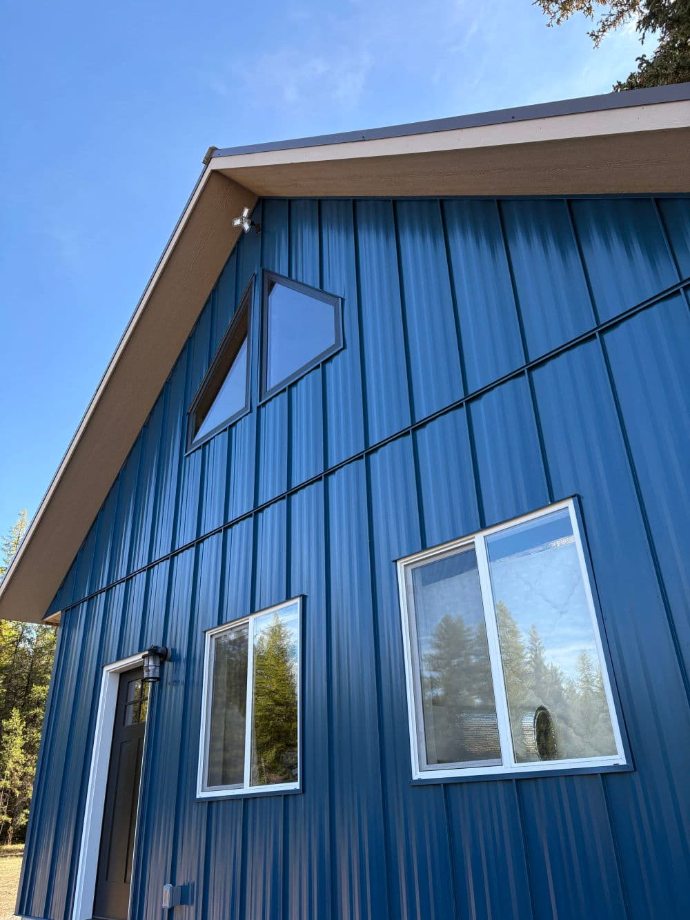 Modern blue metal house exterior with large windows and a clear blue sky.
